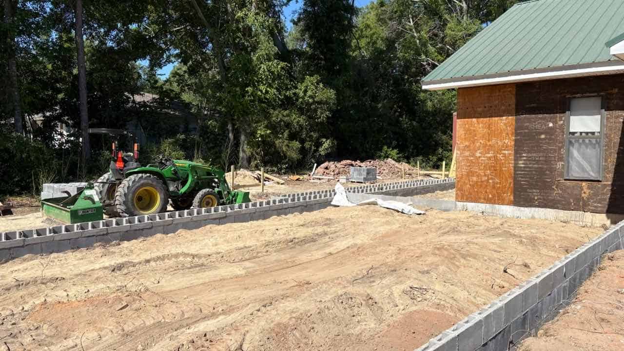 tractor and side of AUUC building with bare graded ground and concrete blocks for beginning construction for an addition to the building