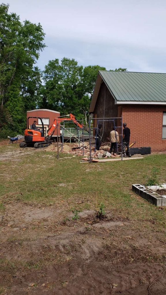 Part of the Aiken UU building, lawn, tractor and 3 construction workers.
